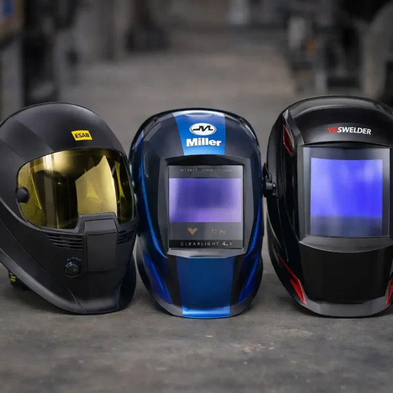 Three auto-darkening welding helmets displayed side by side on a workshop floor, showing different shell designs and viewing lens sizes.